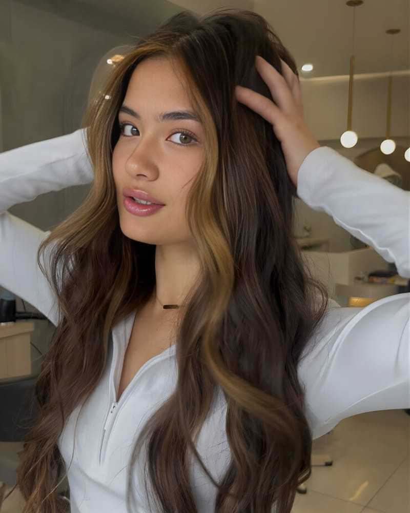 Young woman with long wavy hair posing in a stylish salon setting.