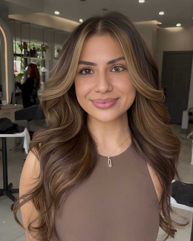 Woman with long, wavy hair and a necklace, standing in a modern salon setting.