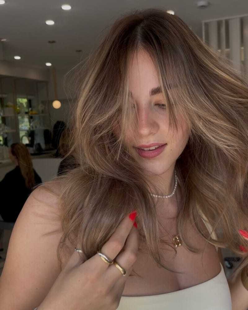 Woman with wavy hair and red nails posing in a brightly lit salon.