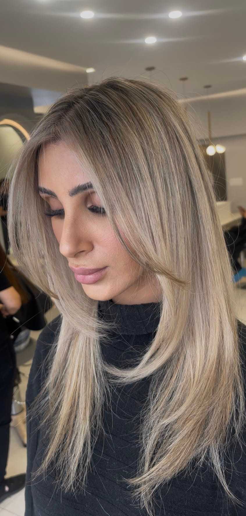 Blonde woman with straight layered hairstyle in a modern salon setting.
