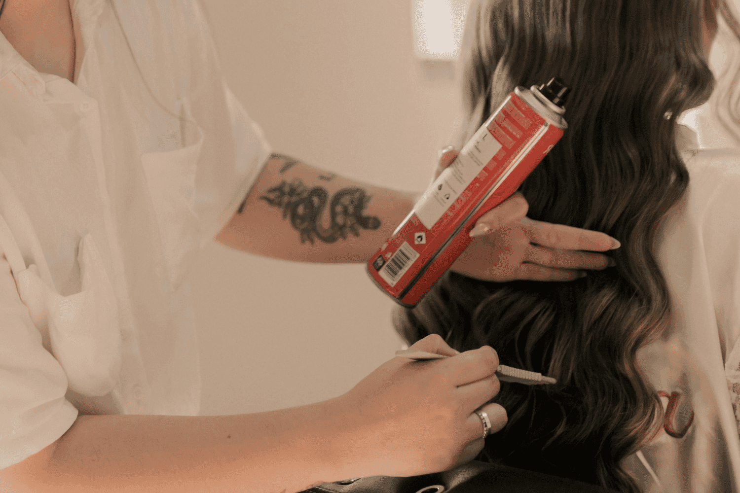 Person styling long hair with a curling iron and hair spray.