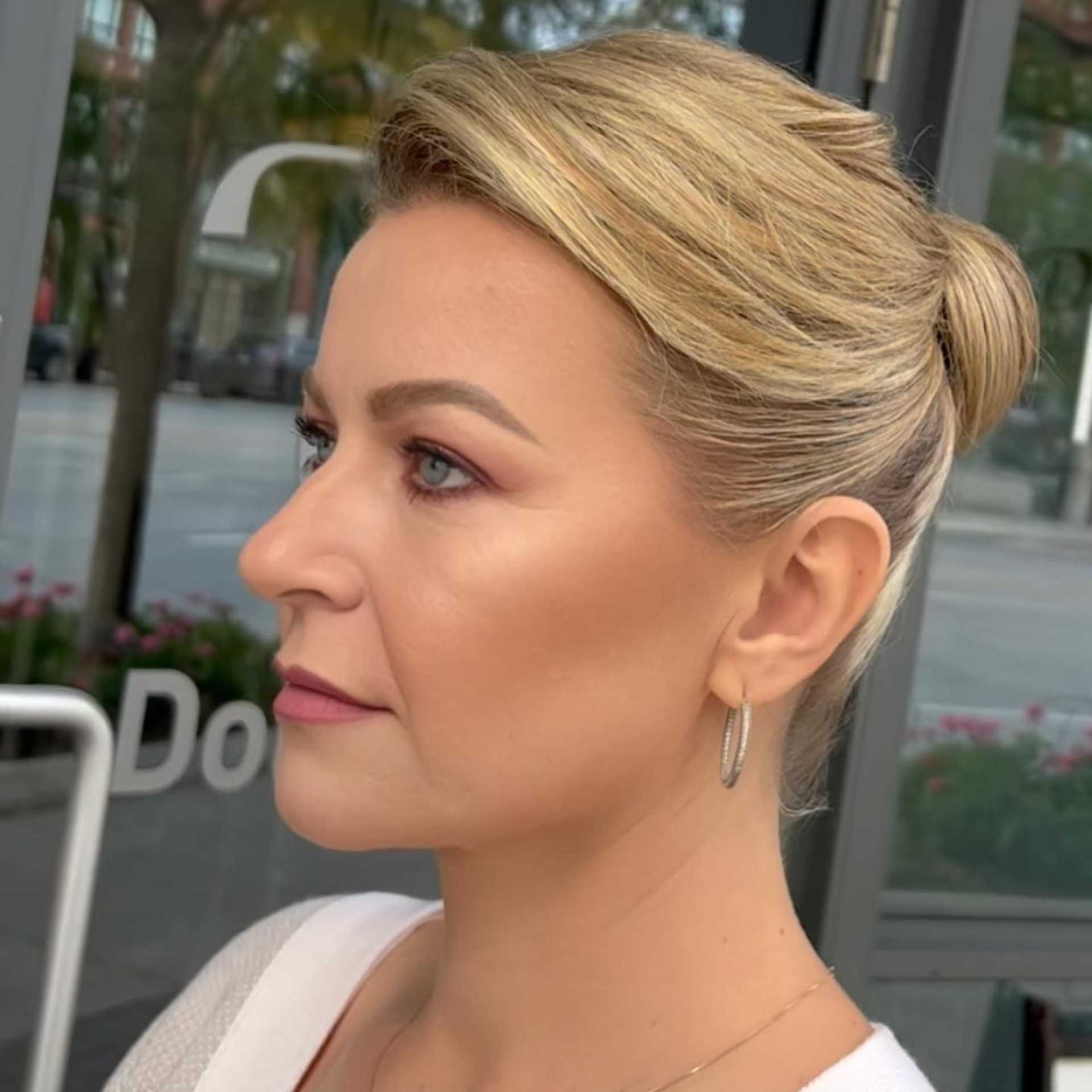 Profile of a person with styled blonde hair, wearing hoop earrings, outside a building.