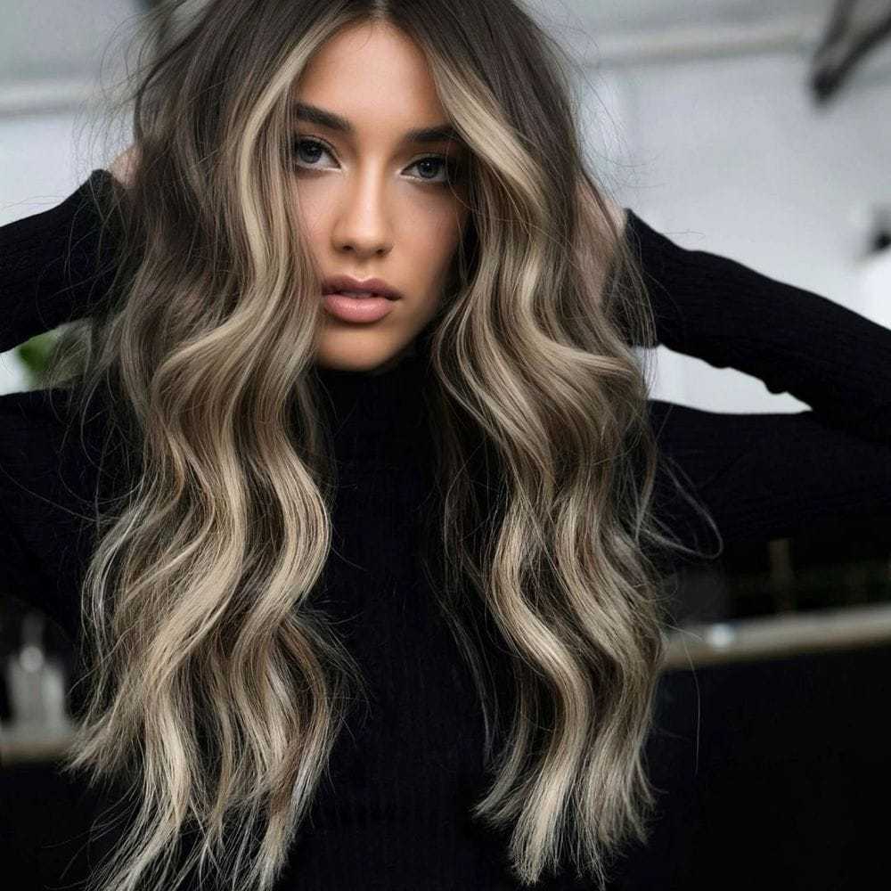 Young woman with long wavy hair and a black sweater, posing indoors.